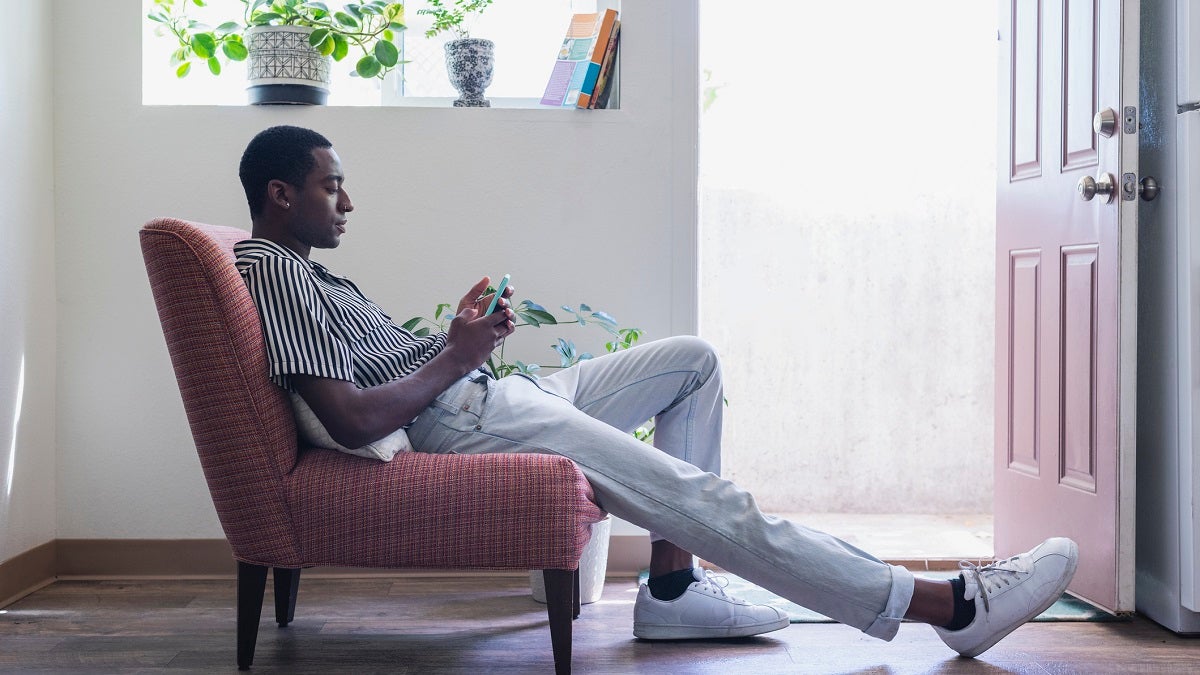 Young man sits in a chair looking at his phone