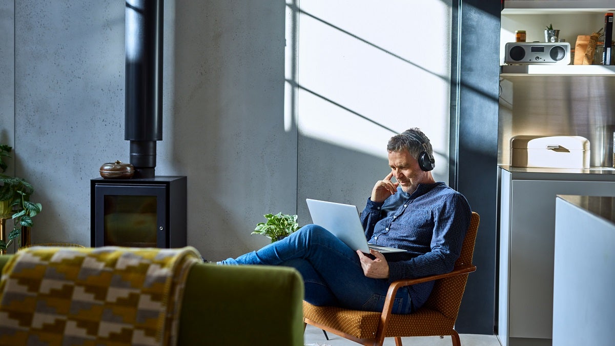 Man siting in armchair looking at laptop with headphones on