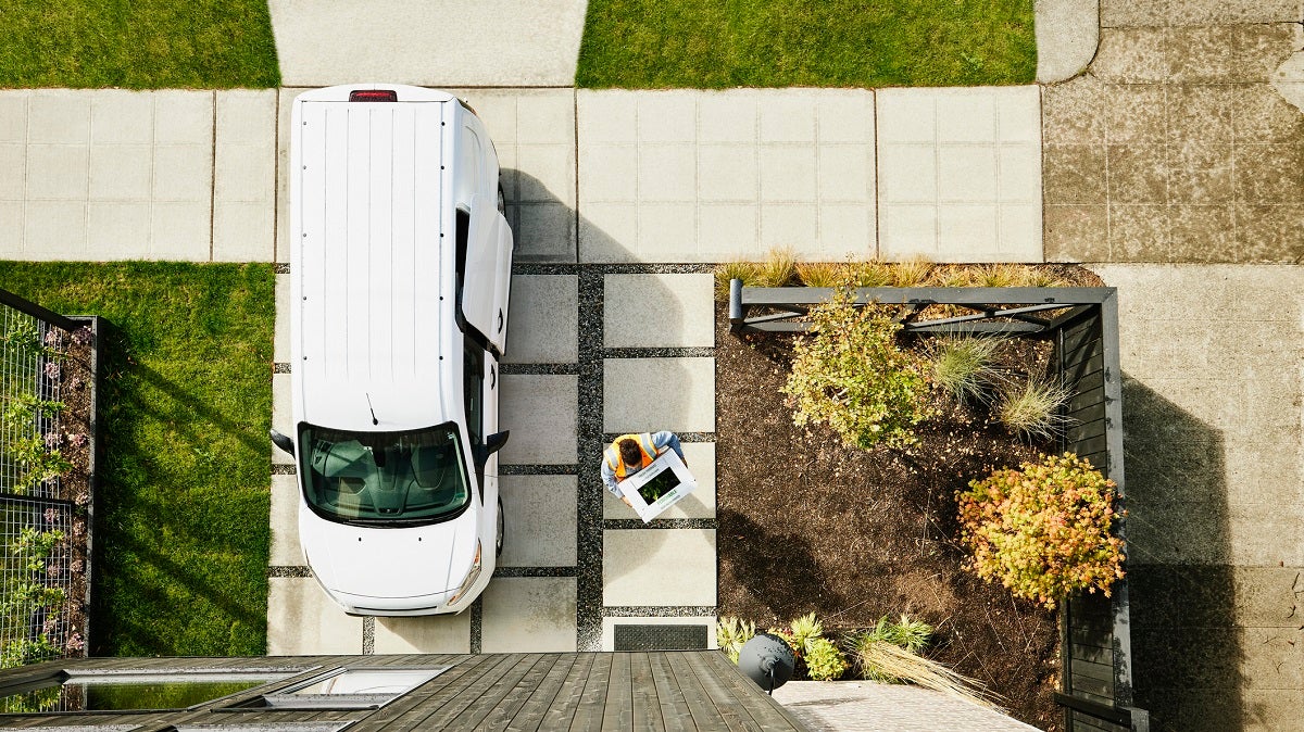 Overhead view of female delivery driver carrying produce box to front door of home