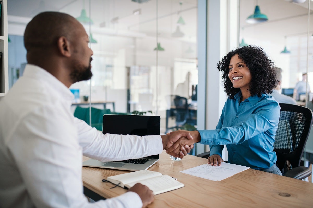 Two people shaking hands over a desk