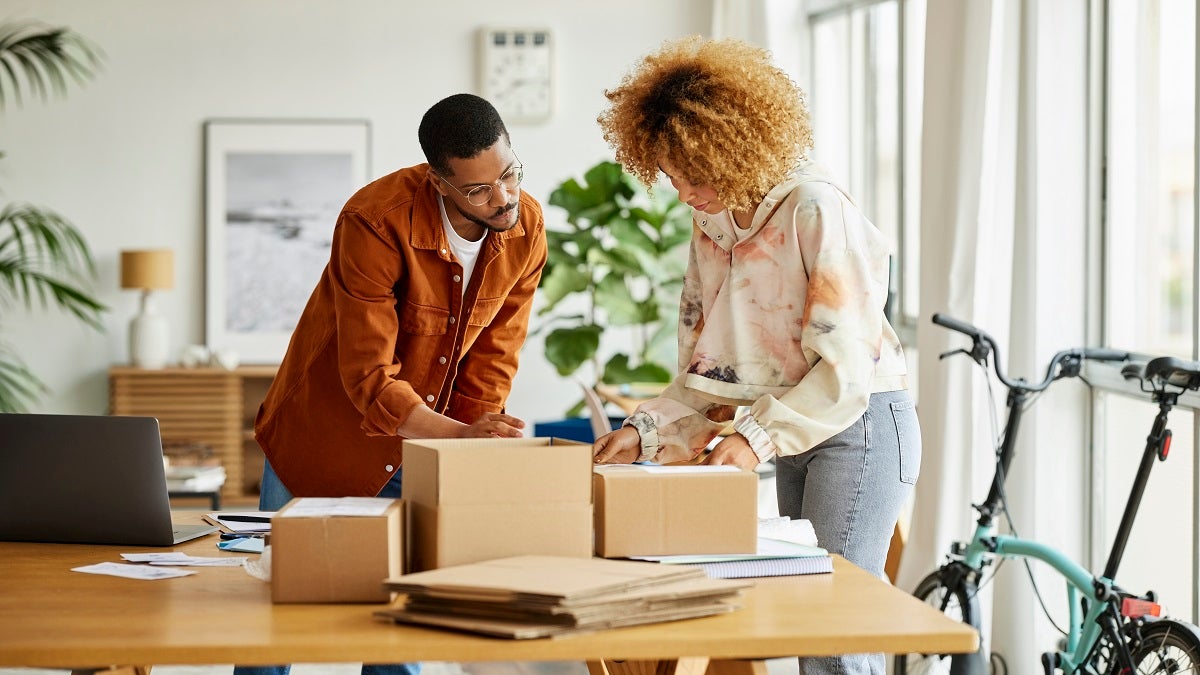 Male and female freelancers analyzing packaging at table. Businessman and businesswoman are working from home office. They are in living room.