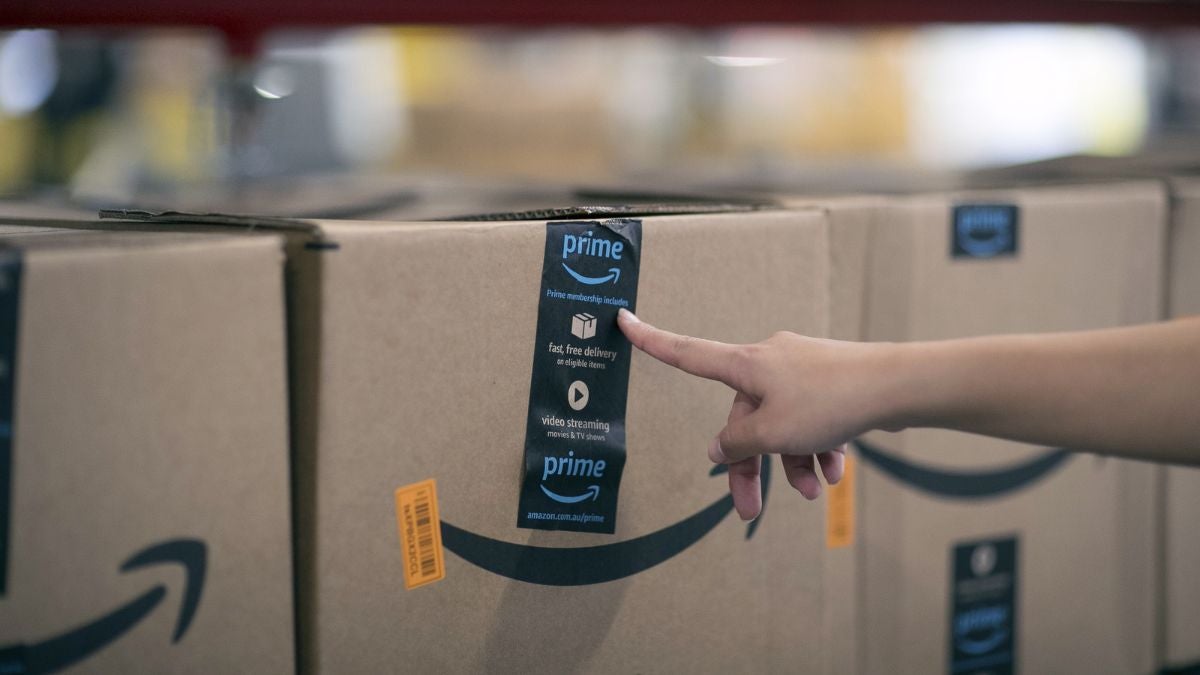 Woman points at line of Amazon-branded boxes lined up in a warehouse