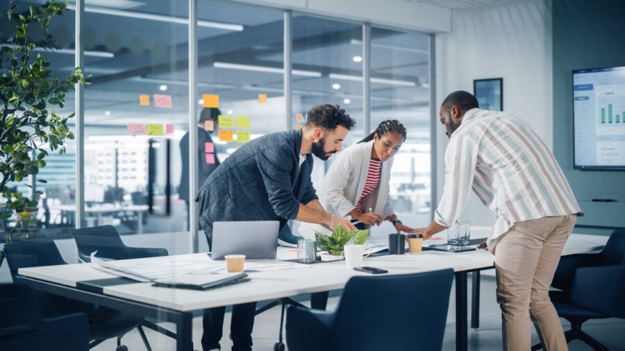 A group of engaged employees stand around a table working together on a project