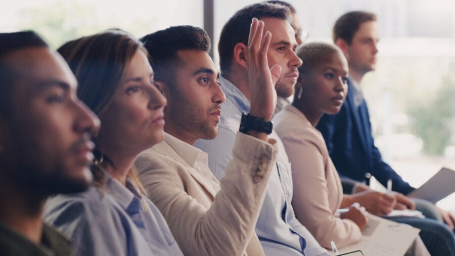 A young employees raises his hand to contribute in a meeting