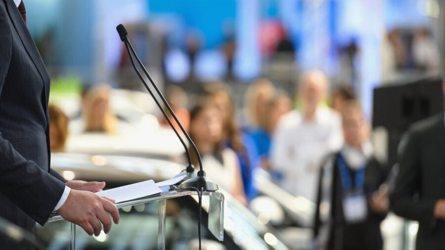 A PR representative speaking to the press from a lectern