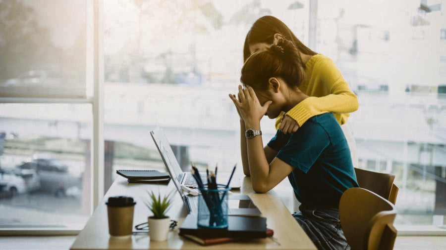 Coworker comforting stressed and discouraged woman in office.