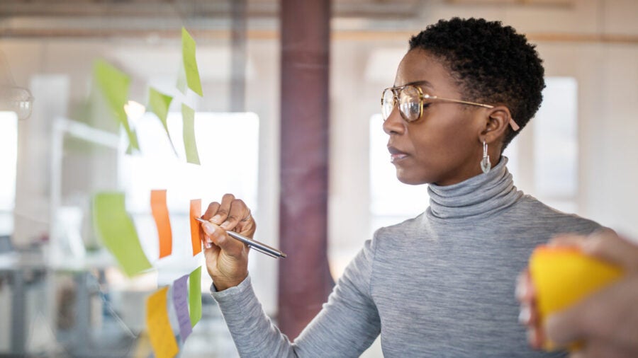 Confident mid adult businesswoman writing new ideas onto a adhesive note over a glass wall.