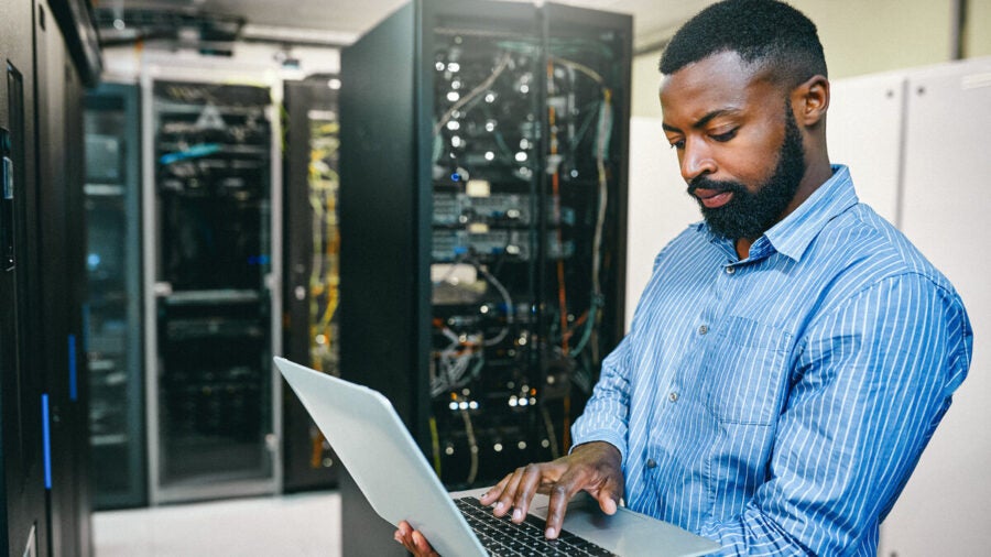 A young man using a laptop while working in a server room