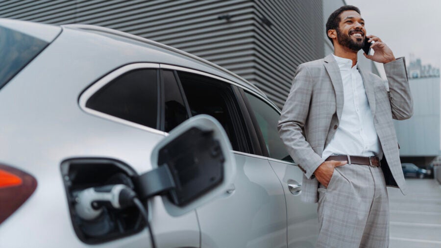 A young business man speaks on the phone while waiting for his EV to charge