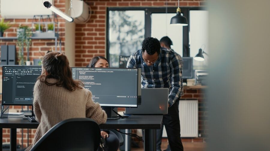 Database Programer Writing Code In Front Of Multiple Computer Screens Displaying Artificial Intelligence